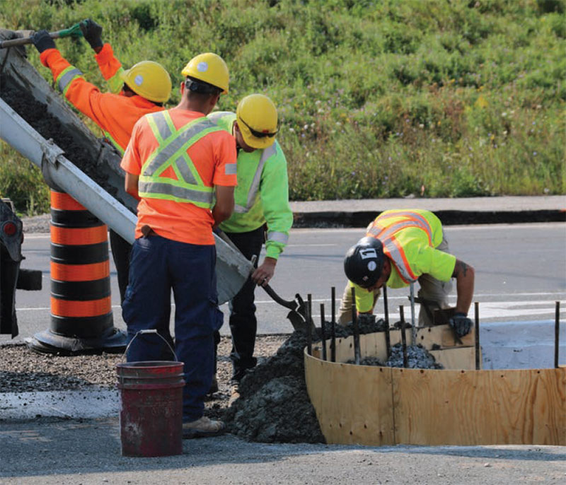 Workers pour concrete around a concrete form.